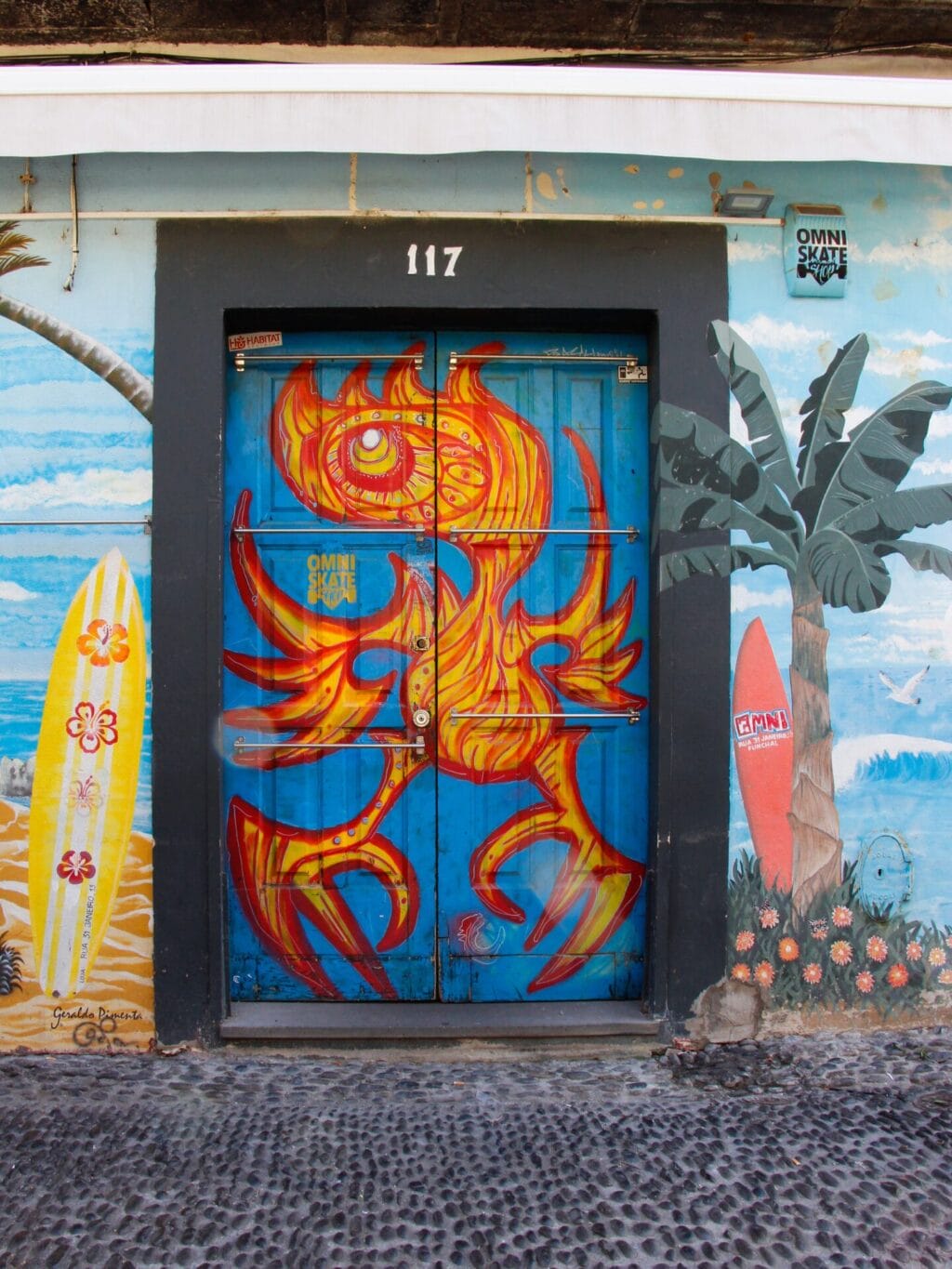 Eine farbenfroh mit Surfbrettern, Palme und stilistischem Vogel bemalte Türe und Wand